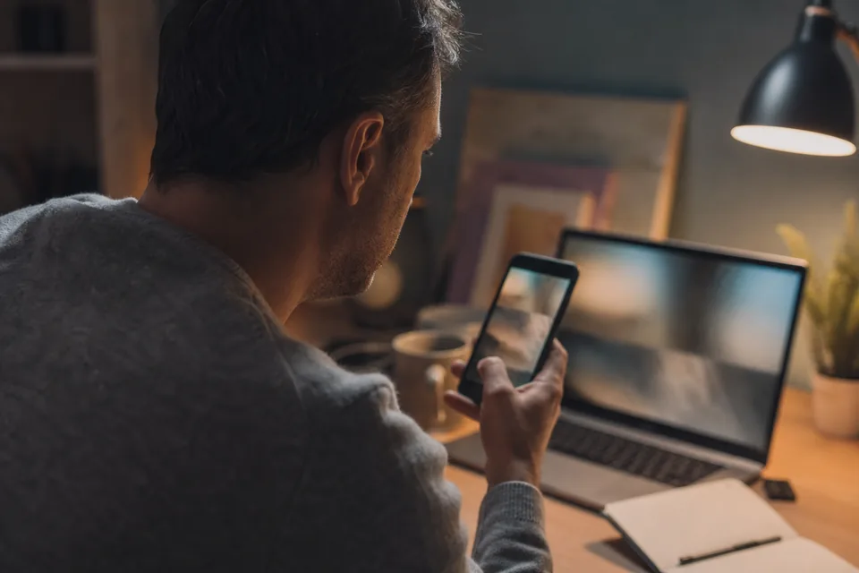Man checking his phone carefully at an evening desk