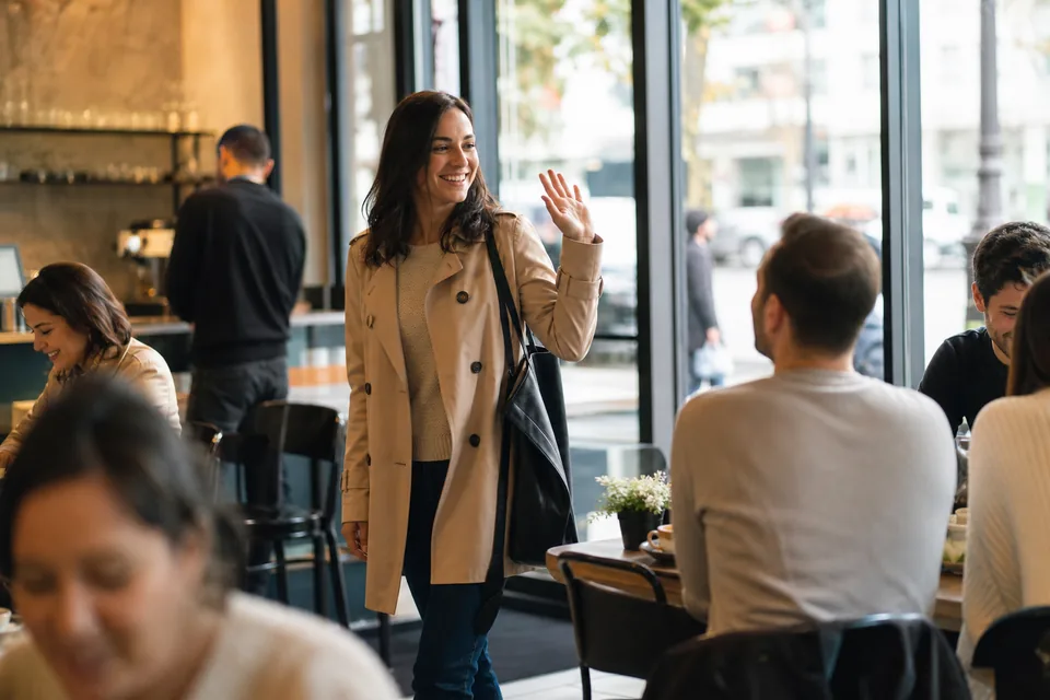 Woman walking into a busy cafe in daylight and waving
