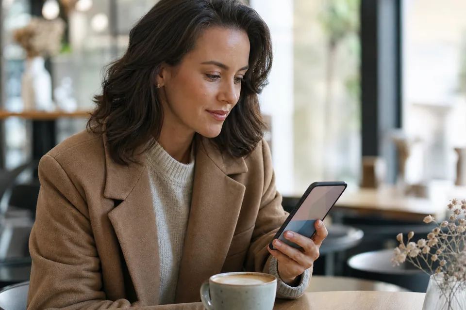 Woman in a camel coat checking her phone calmly at a cafe table